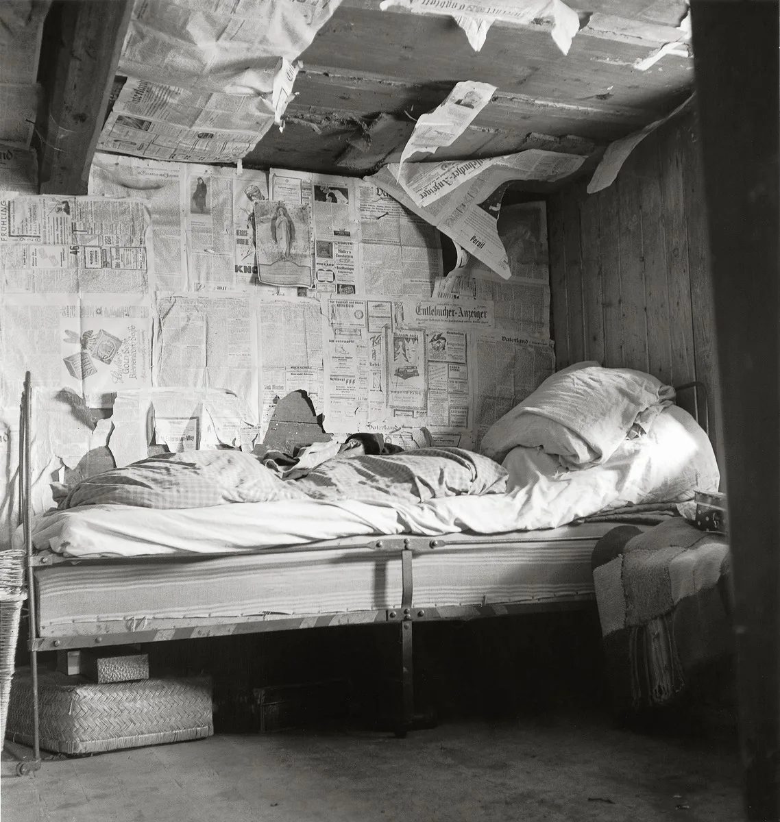 Photographie en noir et blanc. Lit dans une pièce isolée avec de vieux journaux. La photo montre les conditions de vie précaires à Flühli, dans l'Entlebuch (LU), en 1947.