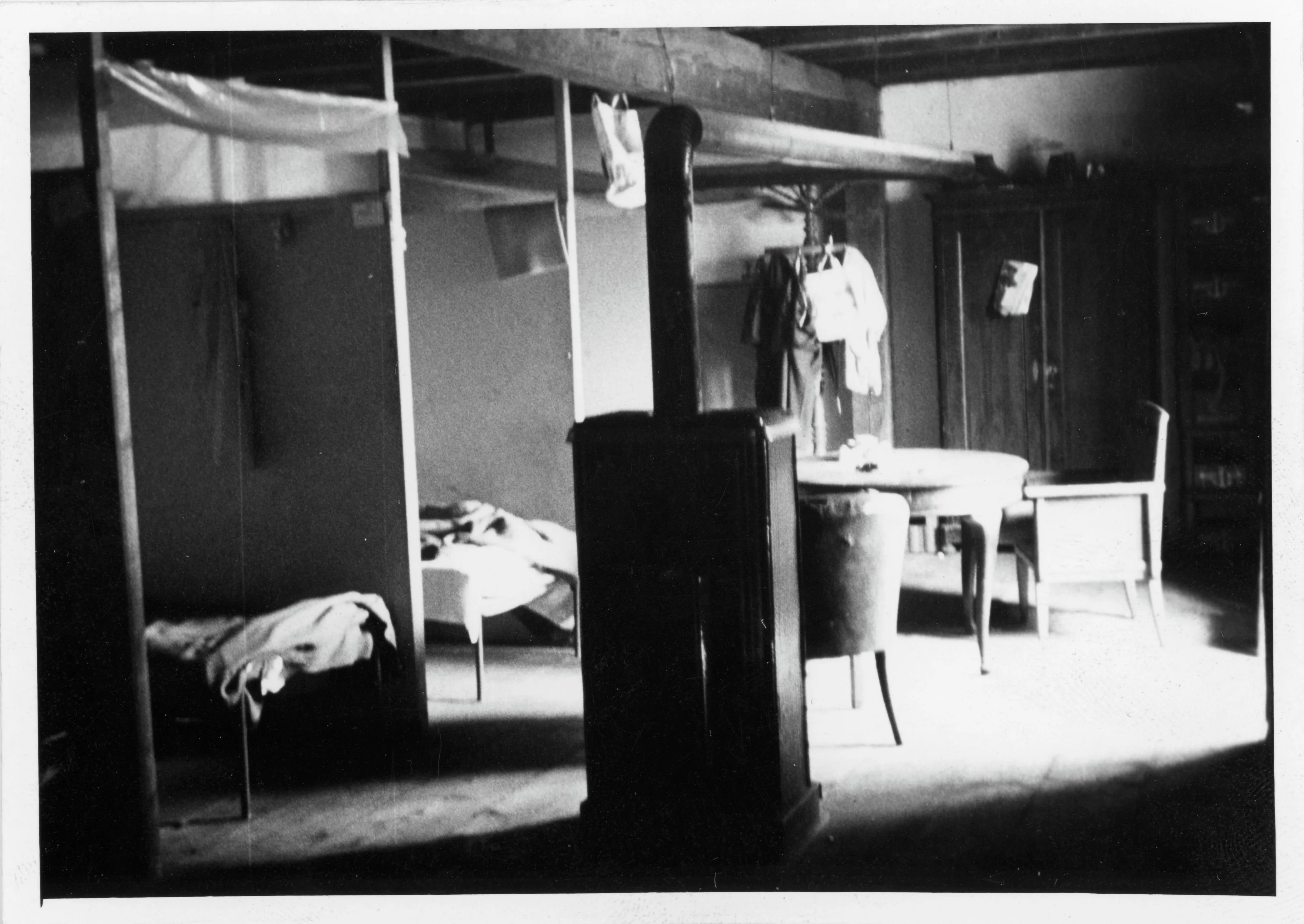 Photographie en noir et blanc d'une pièce avec un poêle, des lits et une table. Il s'agit probablement d'un logement pour saisonniers, 1970. La photo provient des archives du journal « Vorwärts ».