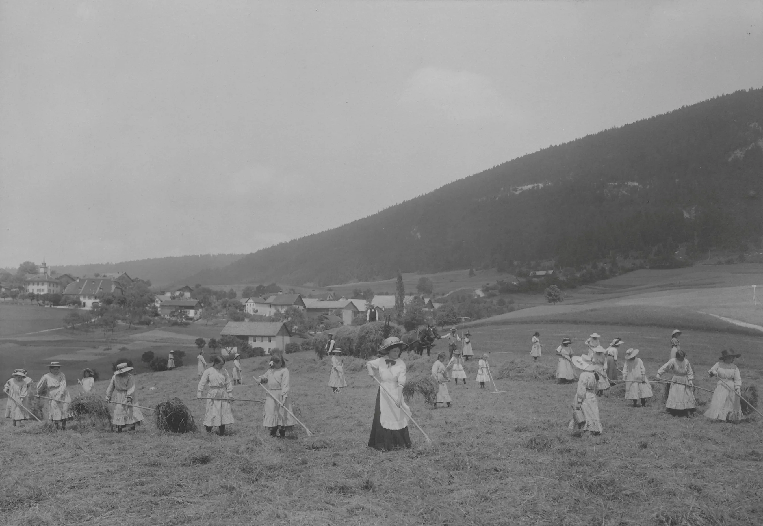 Photographie en noir et blanc de jeunes femmes en habits du dimanche travaillant dans les champs à la maison d'éducation de Loveresse. La photo provient du volume 2 des albums photos de la Direction de l'aide aux indigents du canton de Berne et a été exposée à l'Exposition nationale de 1914 à Berne.